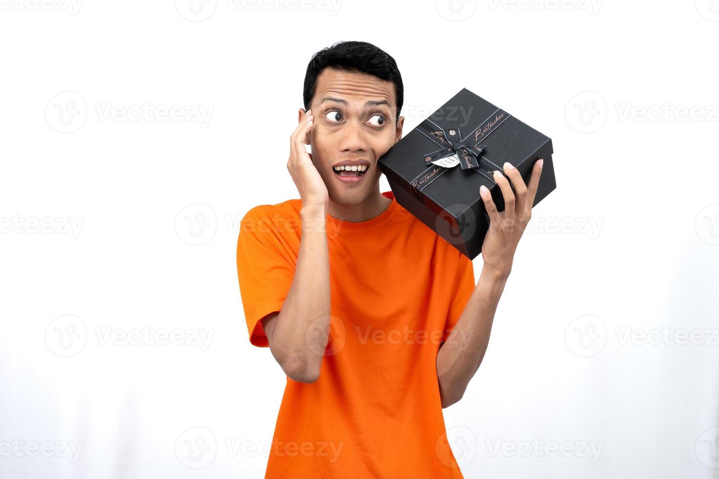 Portrait of a young Asian man wearing an orange t-shirt with a happy expression, surprised to get a gift. Isolated on white background. photo