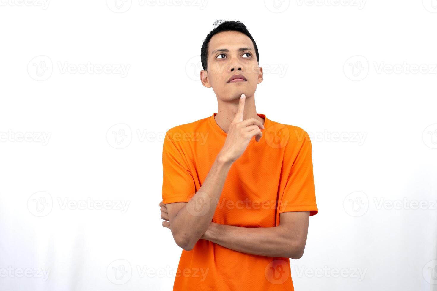 Portrait of a young Asian man wearing an orange t-shirt posing thinking, searching for ideas, or confused. Isolated on white background. photo