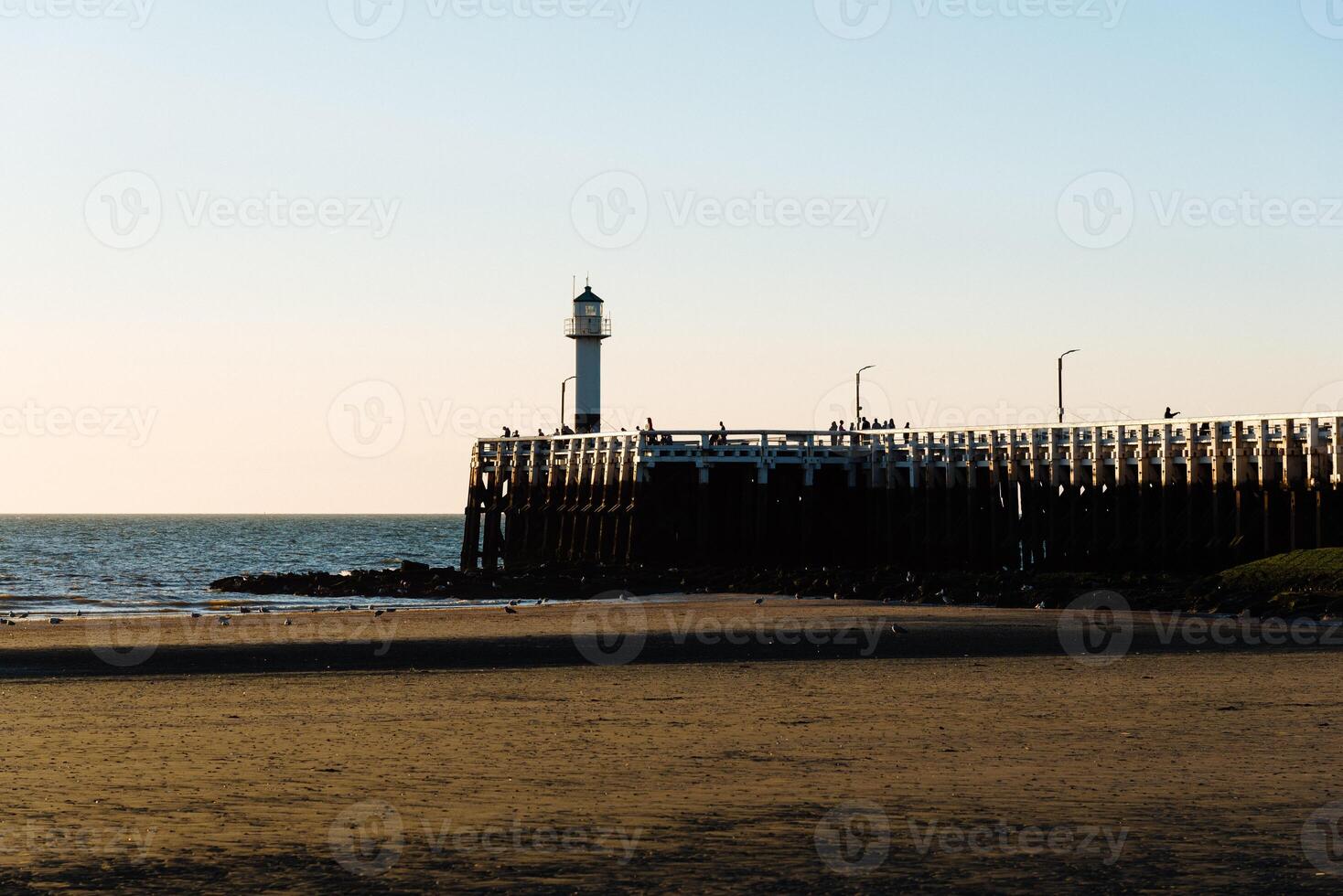 People admiring sunset on the pier with a lighthouse photo