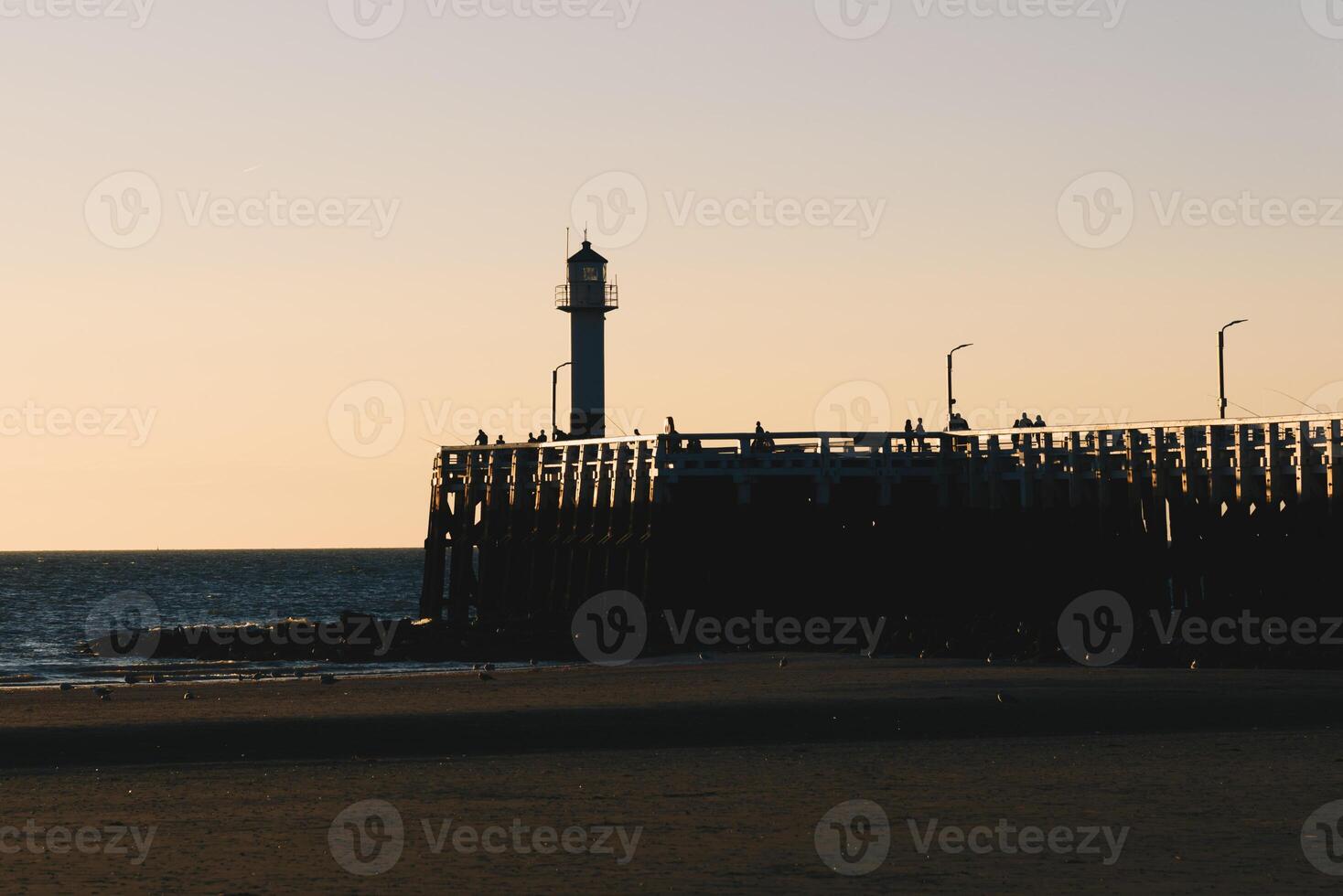 People admiring sunset on the pier with a lighthouse photo