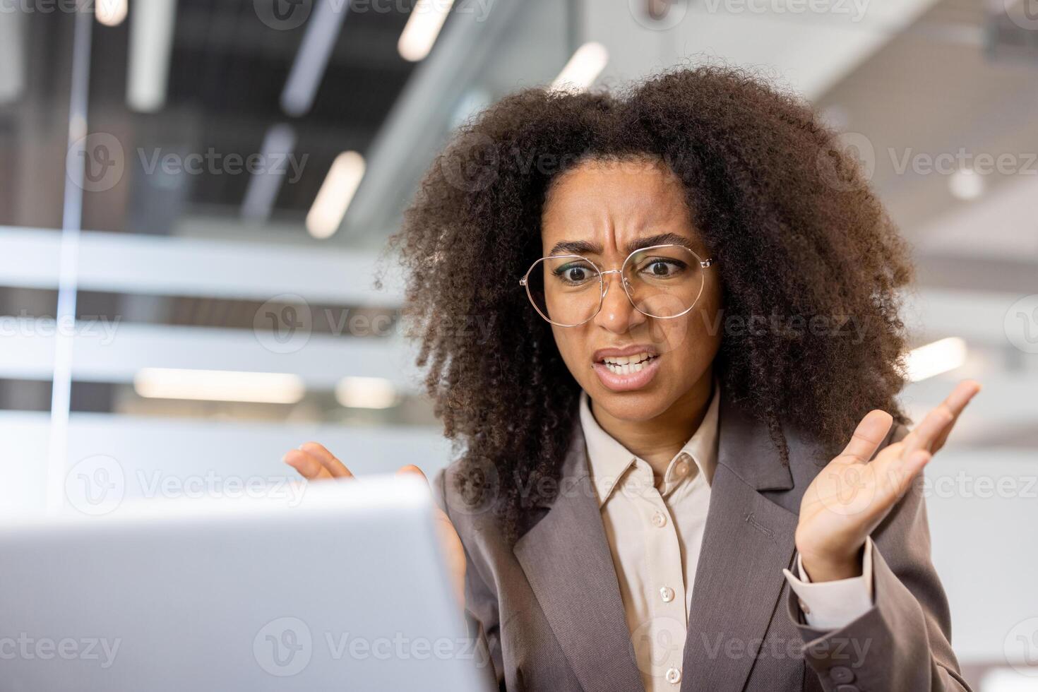 Young African American businesswoman at workplace looking at laptop with confused expression. Concept of business, technology, frustration, problem-solving, and communication. photo