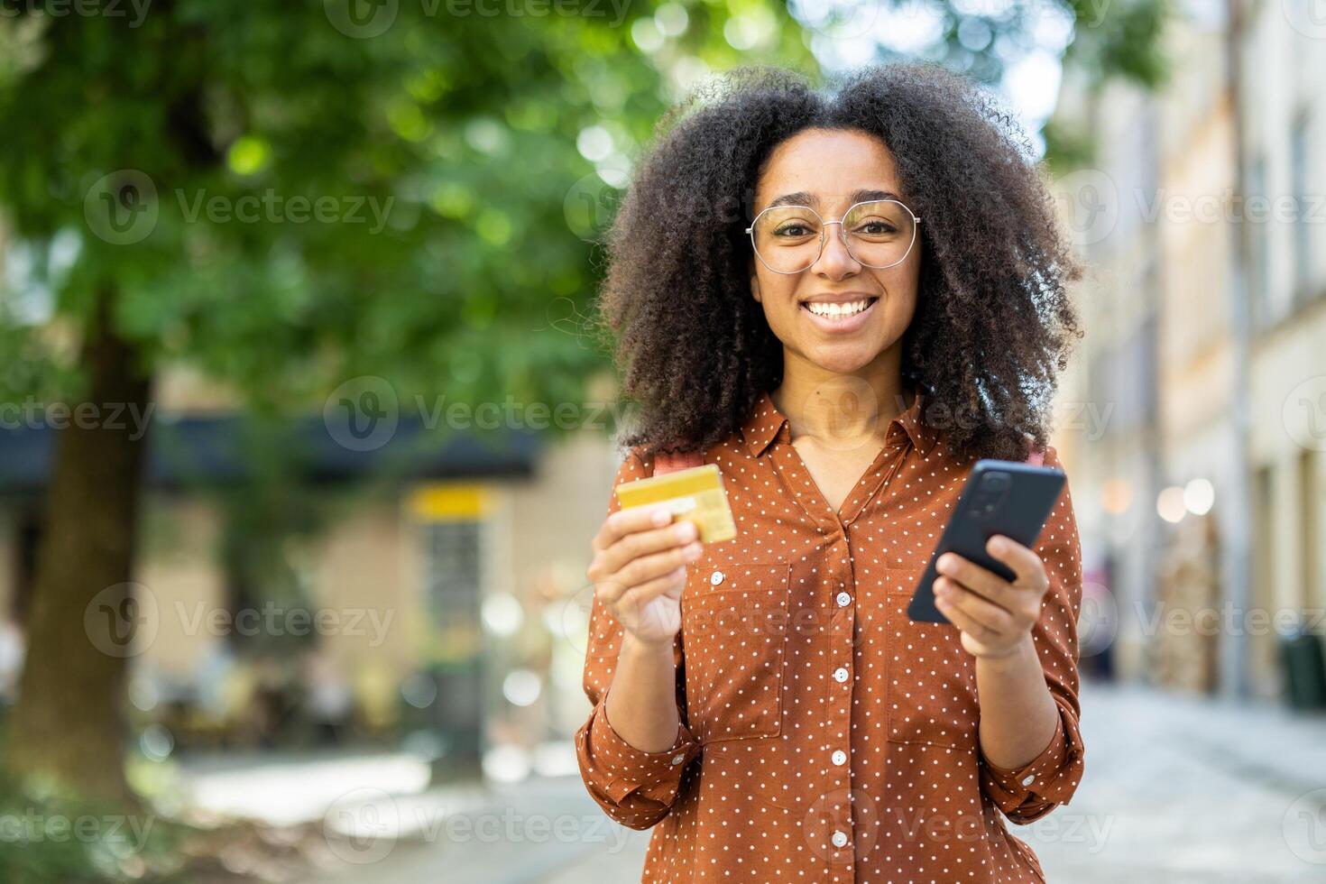 Smiling woman using smartphone for online shopping with credit card outdoors. Digital payment concept shown through confident, happy expression and modern technology use in urban setting. photo