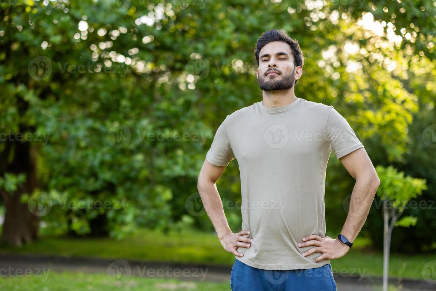 Confident sportsman standing in a park, hands on hips, relishing moment of relaxation. Captures essence of outdoor exercise, fitness routine, mindfulness, and tranquility in natural setting photo