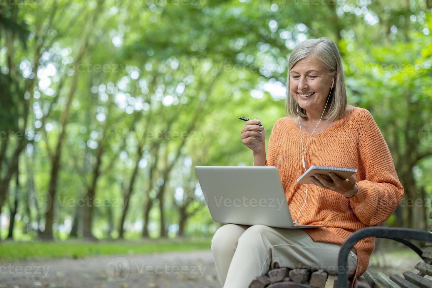 Smiling woman learning online in a serene outdoor environment using laptop and notebook. Capturing knowledge and nature, she enjoys the synergy of technology and tranquility for productive learning. photo