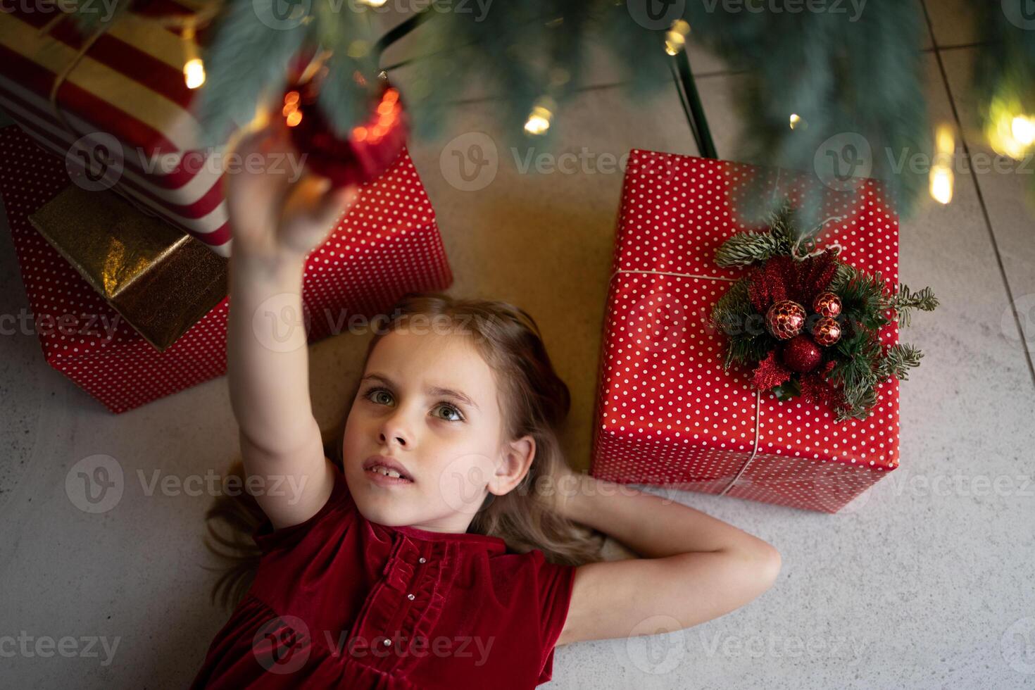 Young girl reaching for ornament under decorated Christmas tree photo