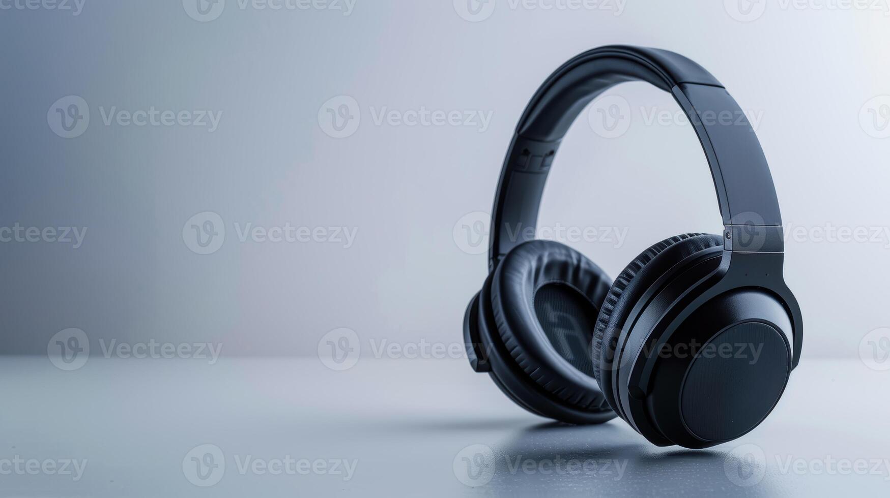 Wireless black headphones with earcups resting on a table against a pale gray backdrop photo