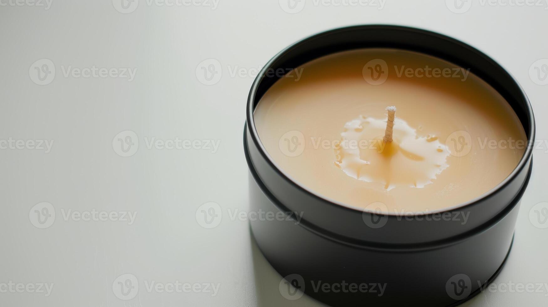 Soy wax candle in a black tin is slowly melting, forming a pool of liquid wax around the wick photo