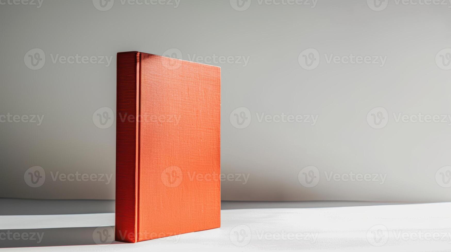 Orange hardcover book standing upright on white surface with gray wall in background photo