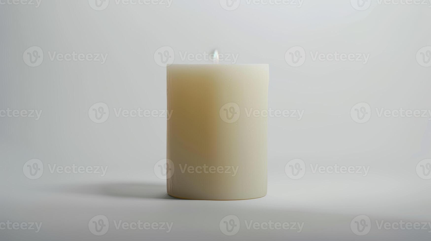 Single white unscented pillar candle is burning on a white background casting a warm glow photo
