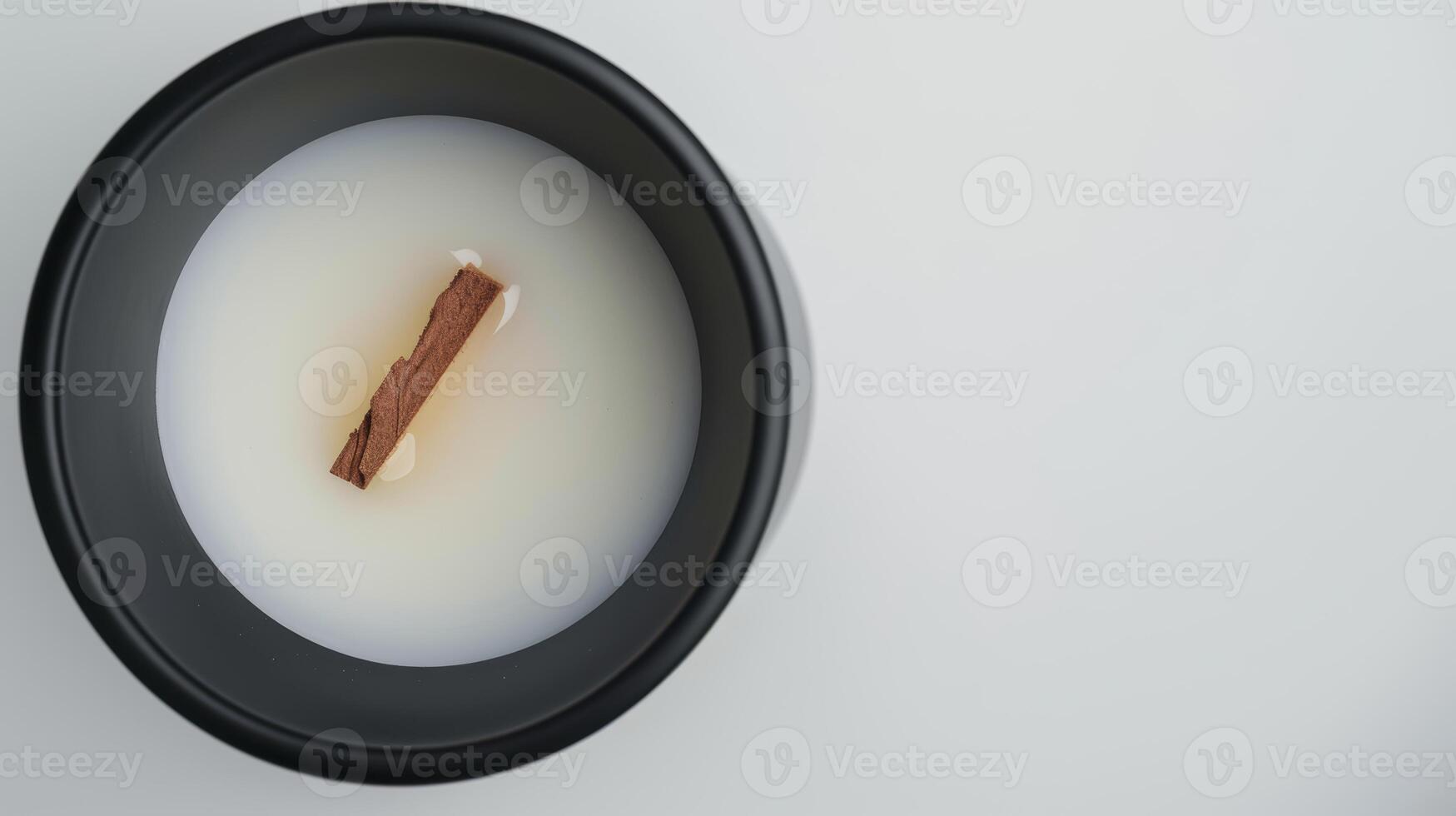 Wooden wick floating in scented candle wax inside a black container on white surface photo