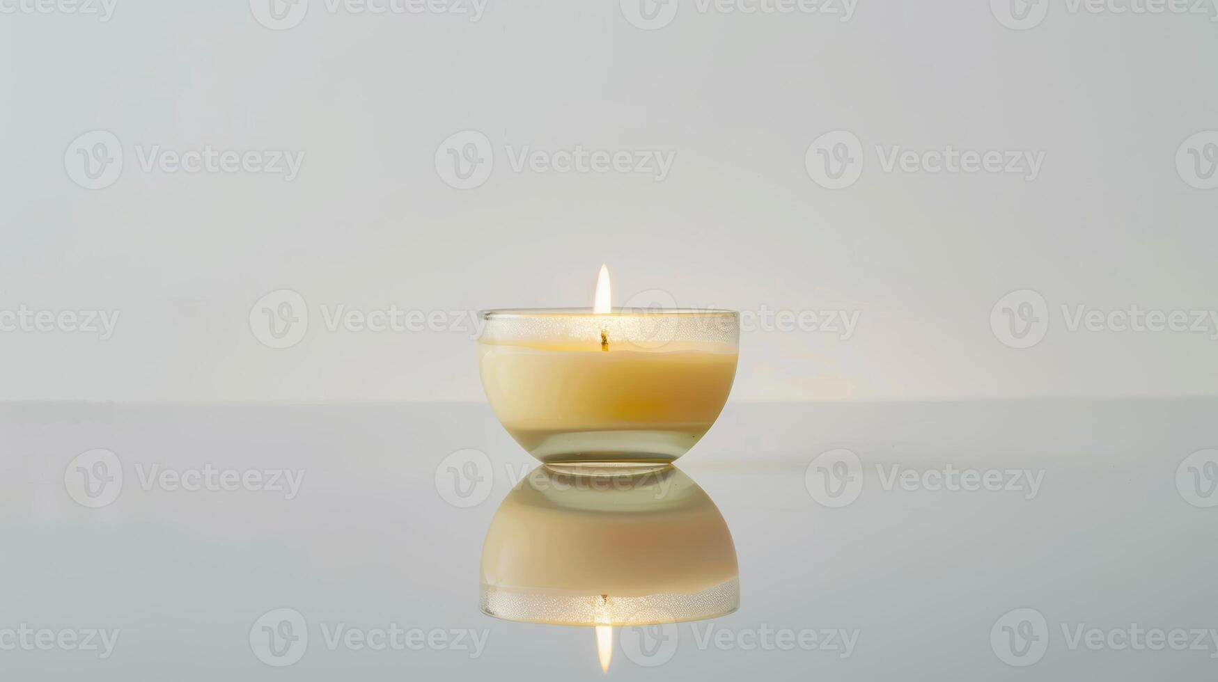 Round candle burns brightly on a reflective surface against a white backdrop photo