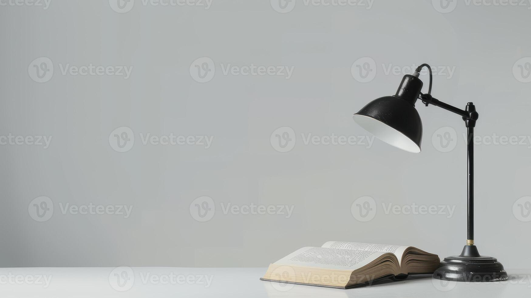 Book illuminated by a black desk lamp on a white table against a grey backdrop photo