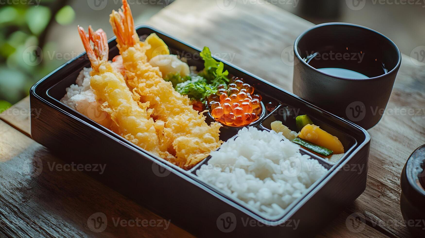 A traditional Japanese bento box filled with tempura shrimp, rice, pickled vegetables, and tamagoyaki, placed neatly on a wooden table with a simple black tea cup photo