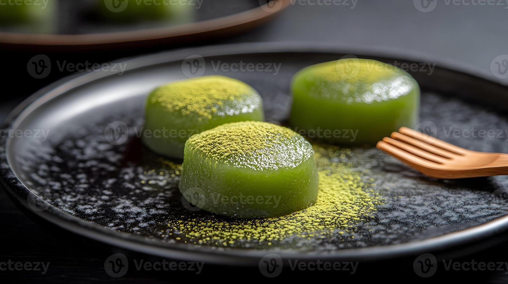 A delicate plate of matcha green tea mochi with powdered matcha dusting the surface, served with a tiny wooden fork on a minimalist black plate photo