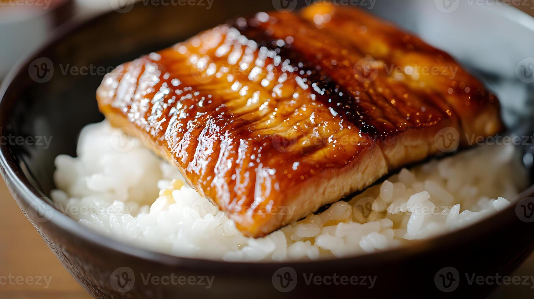 A close-up of a beautifully grilled slice of unagi glazed in sweet soy sauce, placed elegantly over a bed of white rice in a traditional ceramic bowl photo