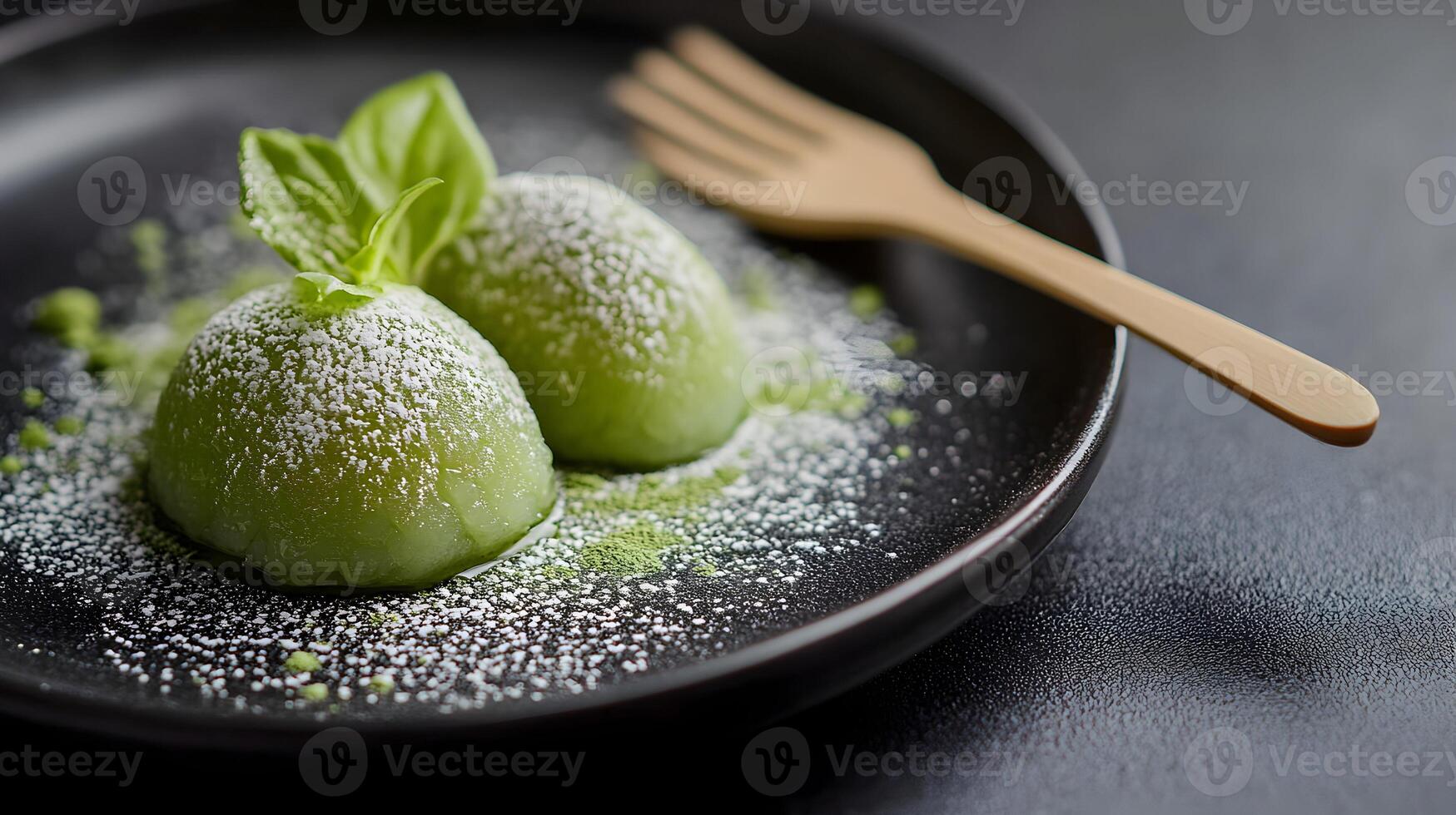 A delicate plate of matcha green tea mochi with powdered matcha dusting the surface, served with a tiny wooden fork on a minimalist black plate photo