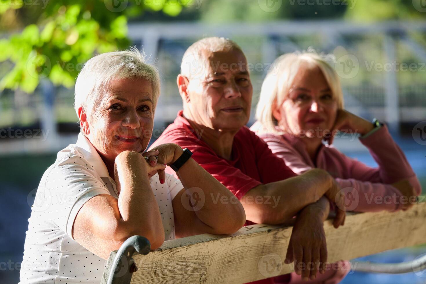 A group of elderly individuals, including a senior man and two older women, sits in a park on a sunny autumn day, embodying the concept of healthy aging through companionship, relaxation, and outdoor photo