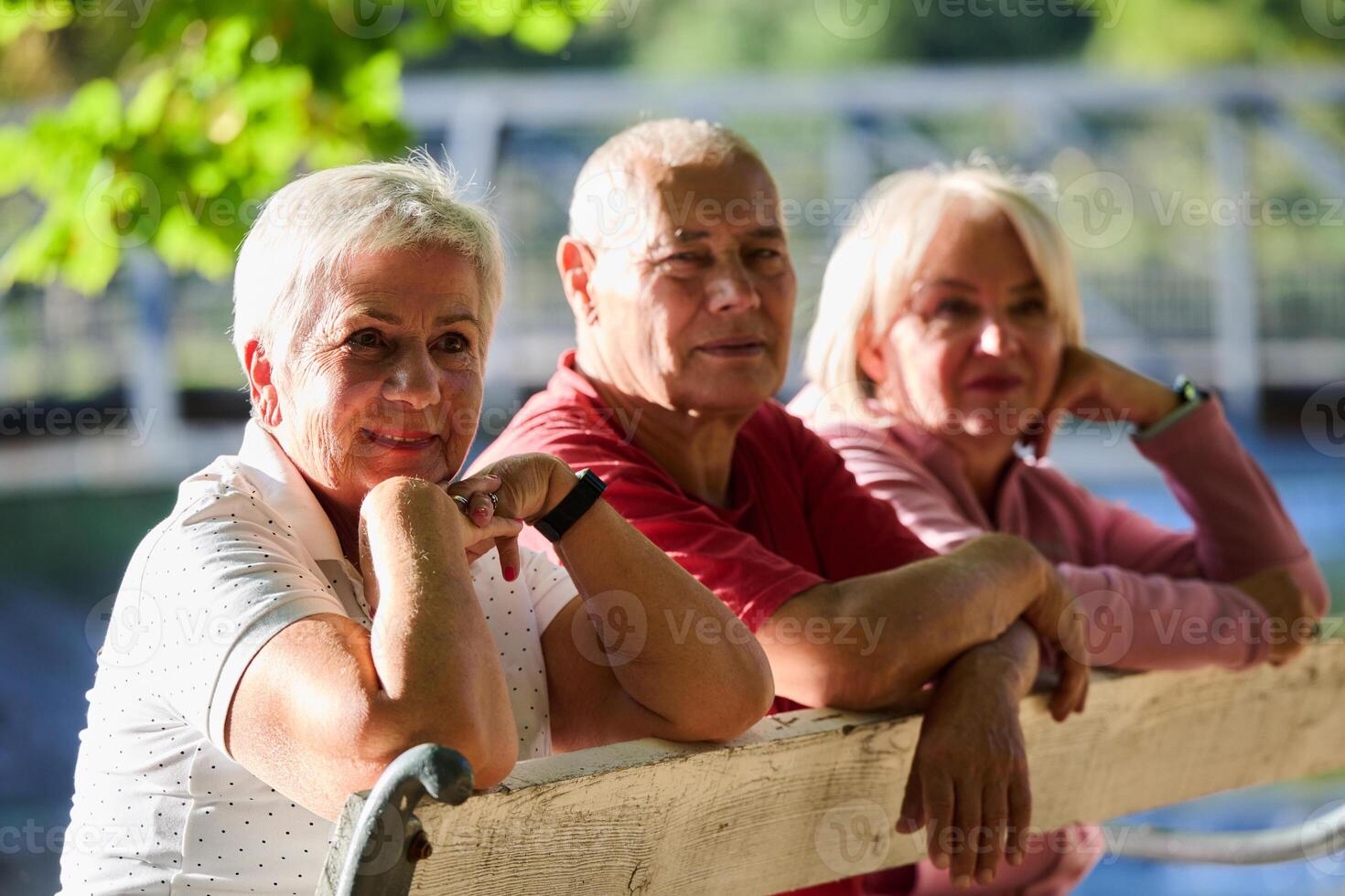 A group of elderly individuals, including a senior man and two older women, sits in a park on a sunny autumn day, embodying the concept of healthy aging through companionship, relaxation, and outdoor photo