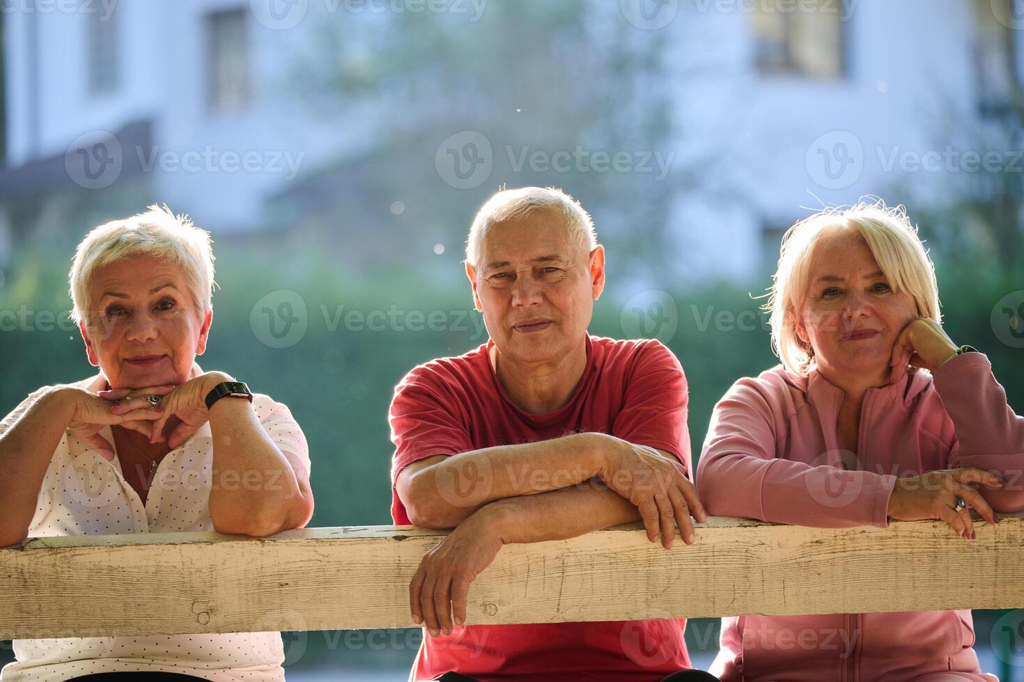 A group of elderly individuals, including a senior man and two older women, sits in a park on a sunny autumn day, embodying the concept of healthy aging through companionship, relaxation, and outdoor photo