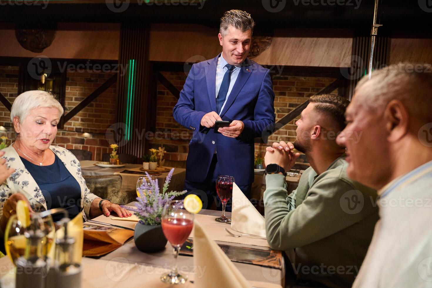 A courteous waiter provides impeccable service to an elderly family and their friends, creating a convivial atmosphere as they gather for a shared lunch, indulging in the diverse and delectable photo