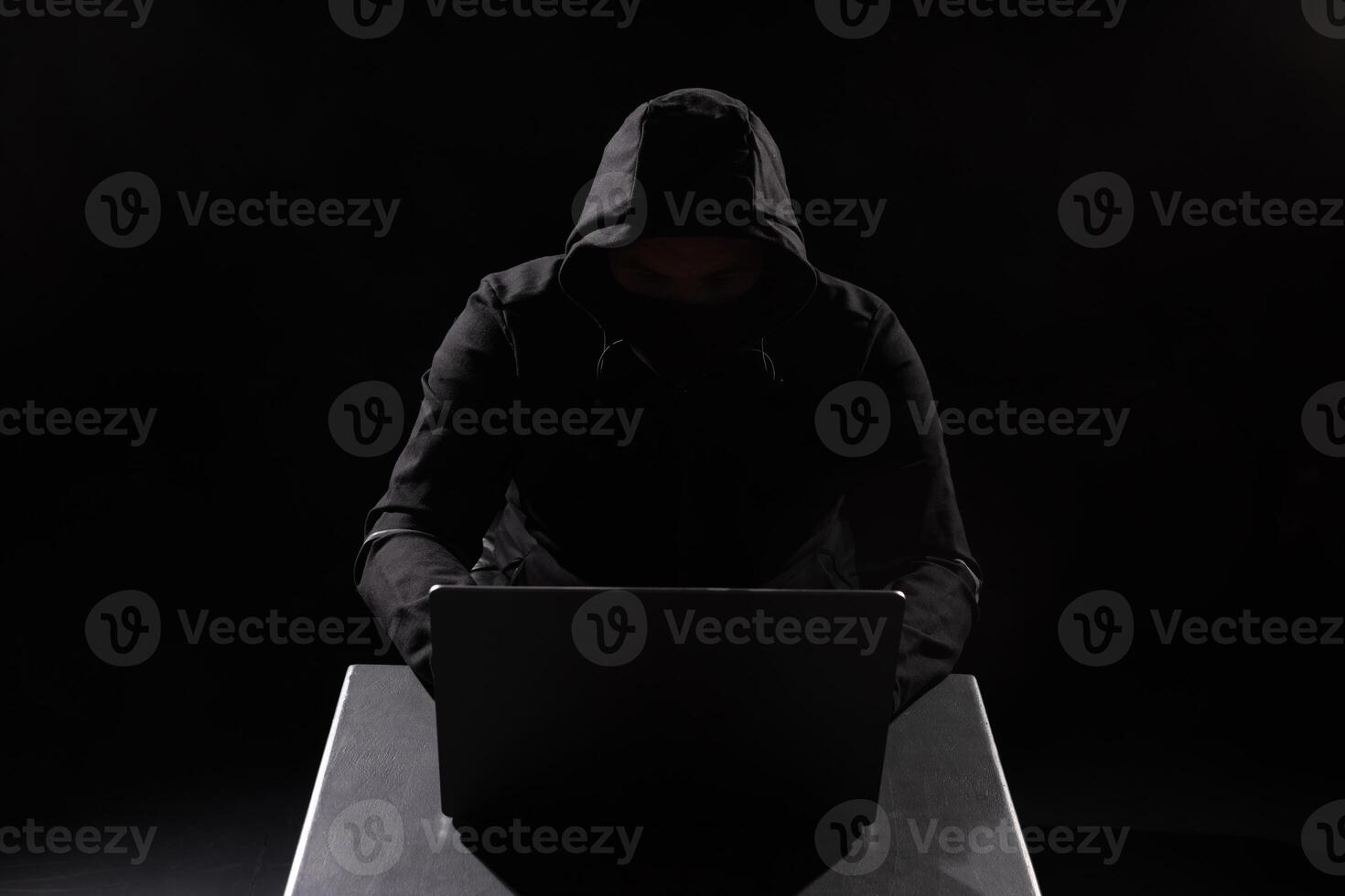 Cyber hacker in hood behind laptop in dark room, digital cyber security concept, Computer hacking photo