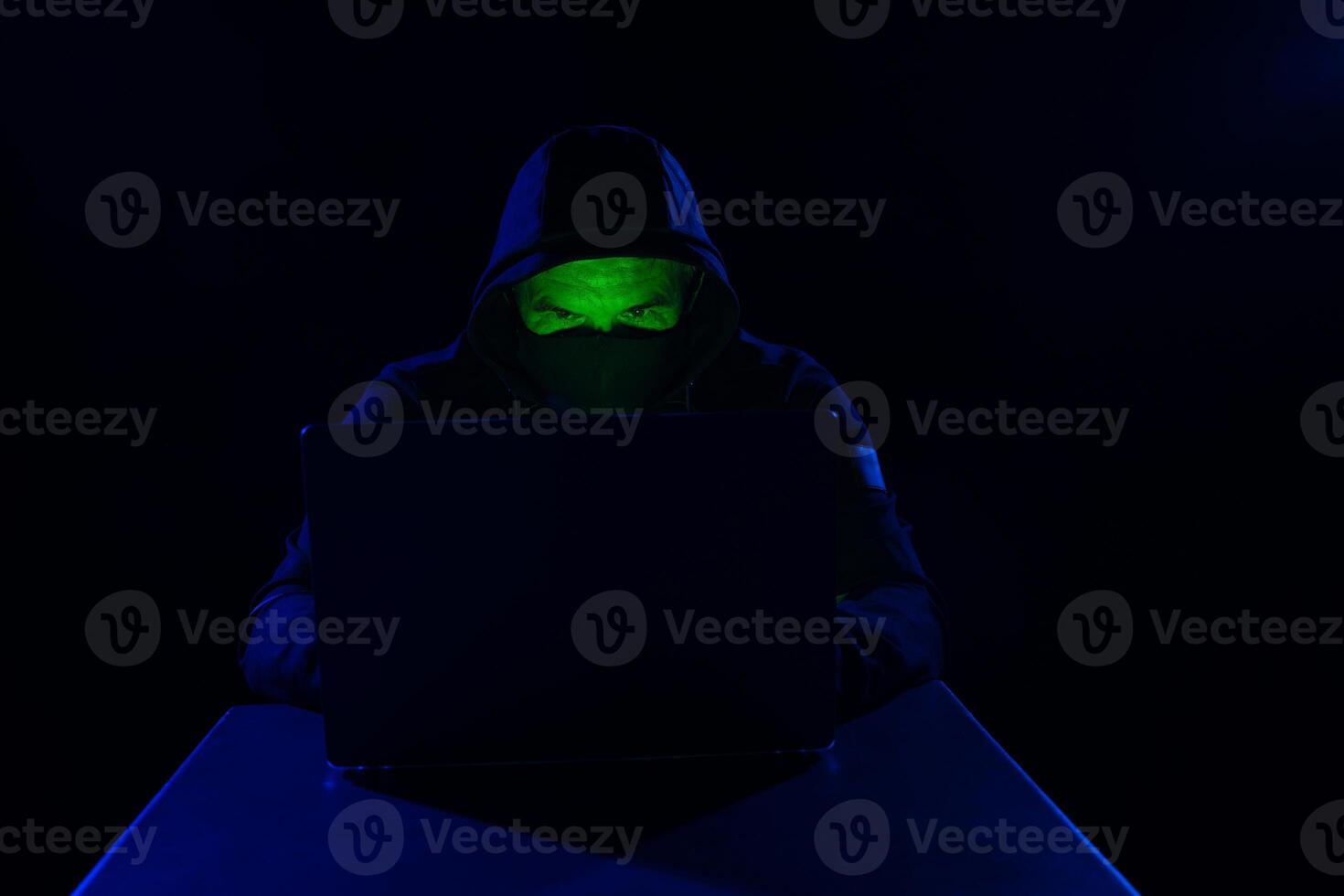 Cyber hacker, digital cyber security concept, hooded hacker behind laptop on dark background photo