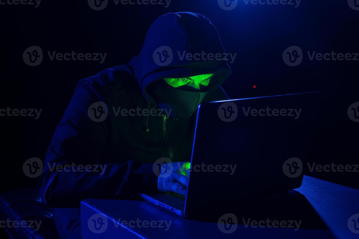 Cyber hacker in hood behind laptop in dark room, digital cyber security concept, Computer hacking photo