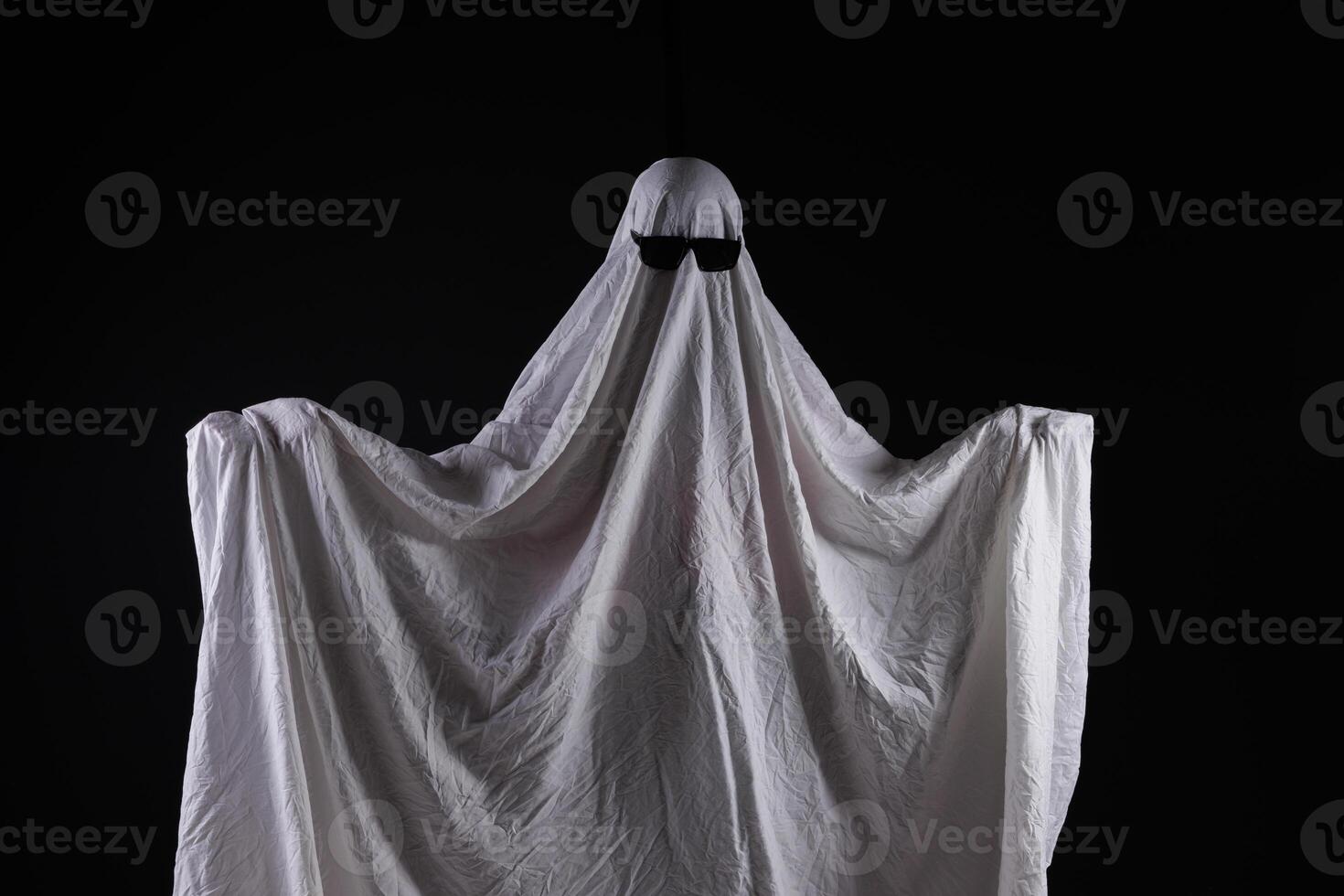 Person in costume of ghost pointing at something on dark background with space for tex photo