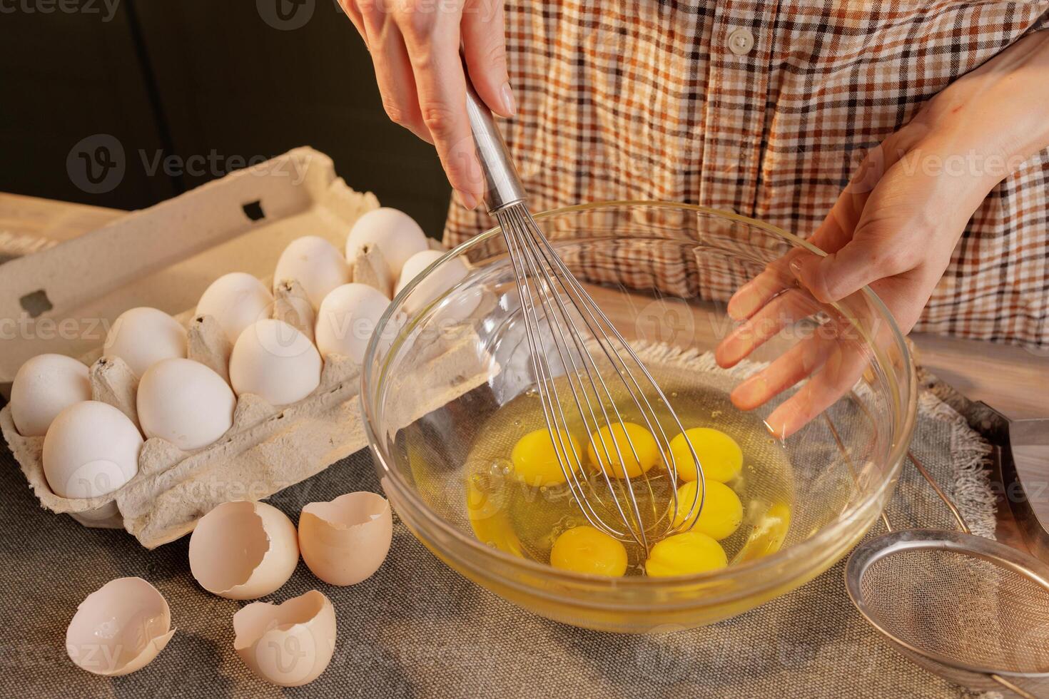 Close-up of female hands beating eggs with a hand whisk in a transparent bowl against photo