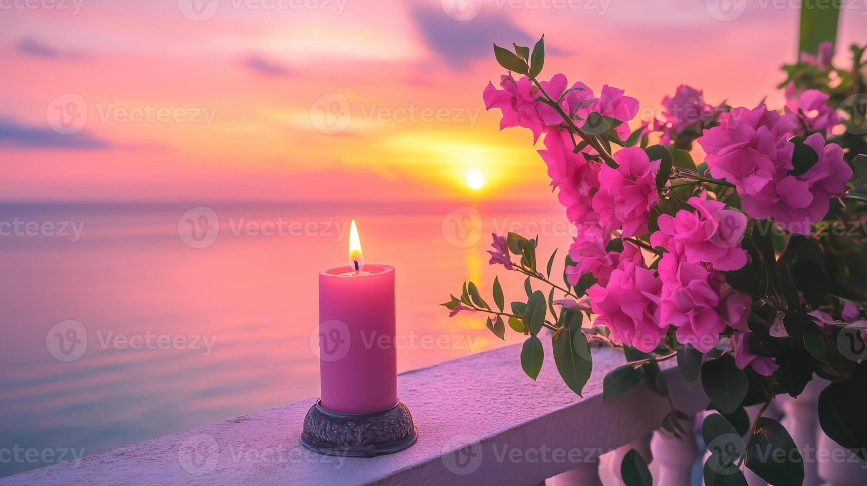 A pink candle and vibrant flowers on a balcony overlook a serene sunset photo