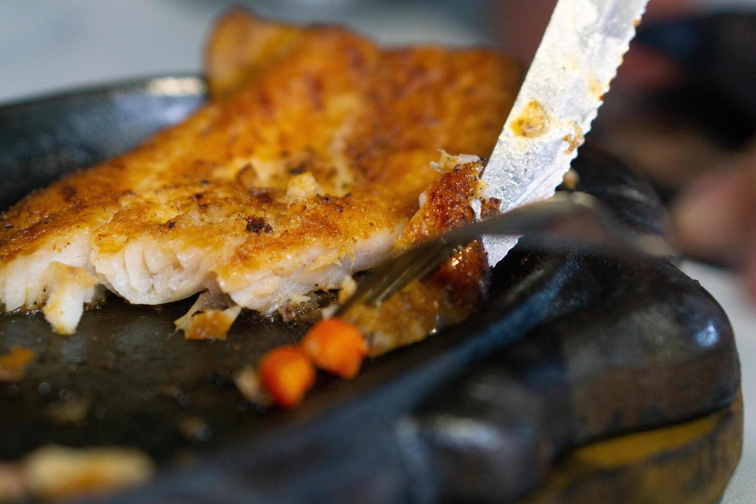 Close up of Cutting or slicing the dori steak on grill plate with knife and fork photo