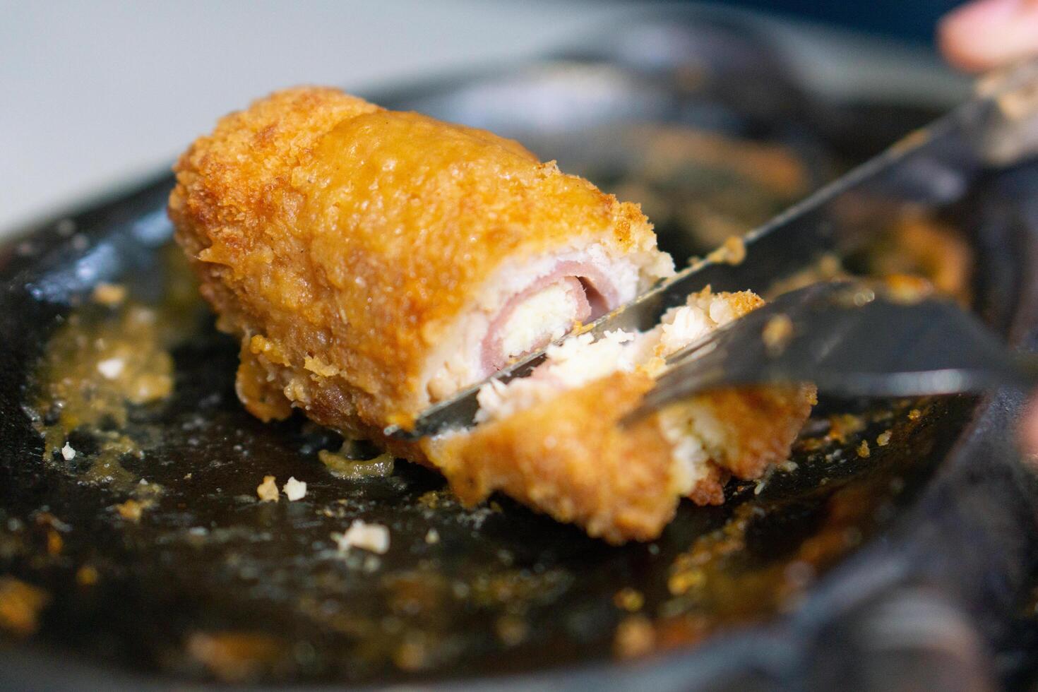 Close up of sliced chicken cordon blue with knife and fork on grill plate photo