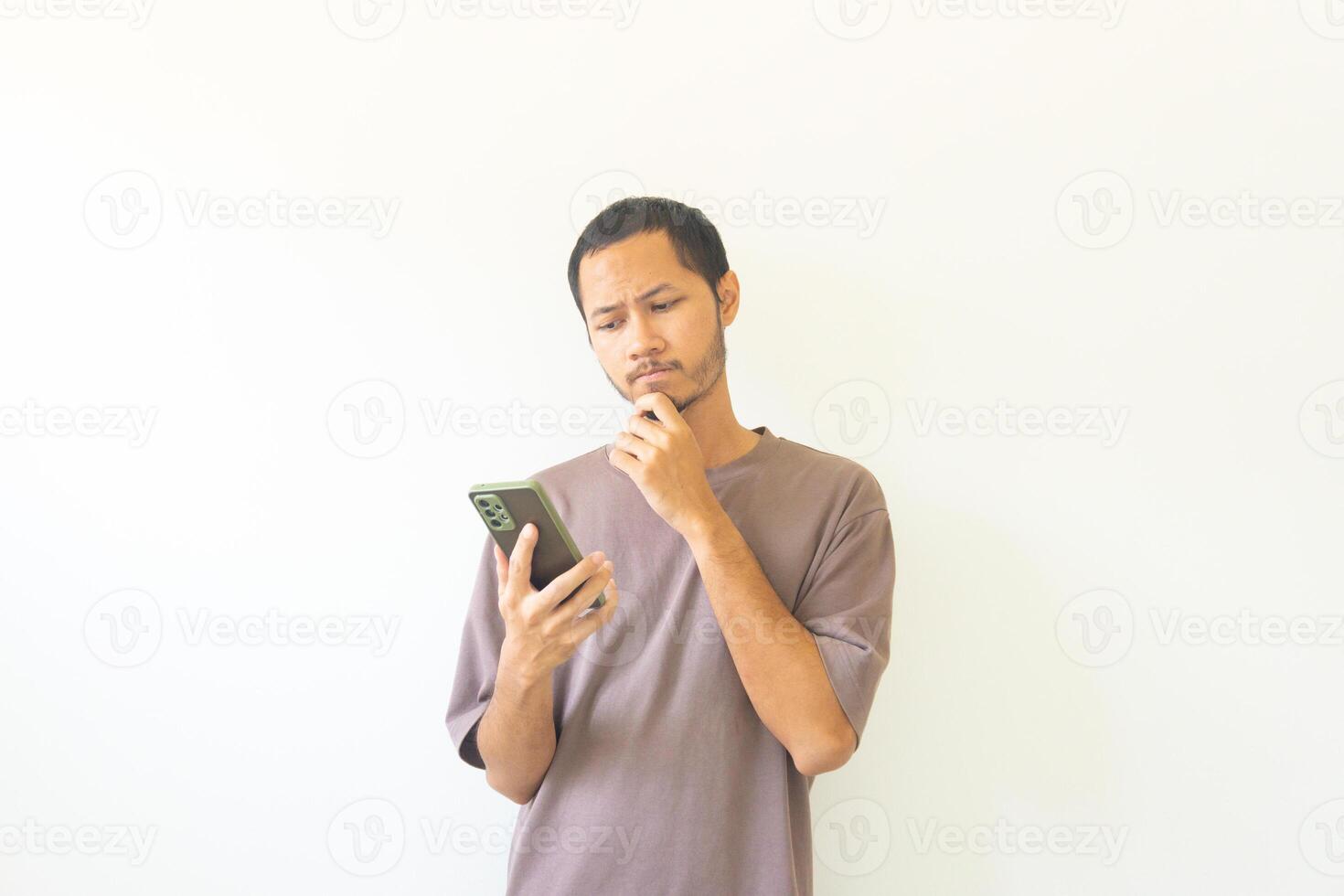 Pensive young asian men is thinking while holding smathphone on isolated white background photo