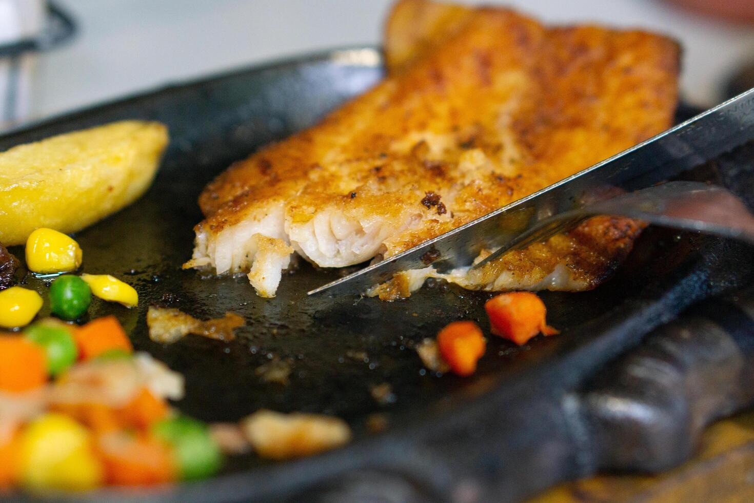 Close up of Cutting or slicing the dori steak on grill plate with knife and fork photo
