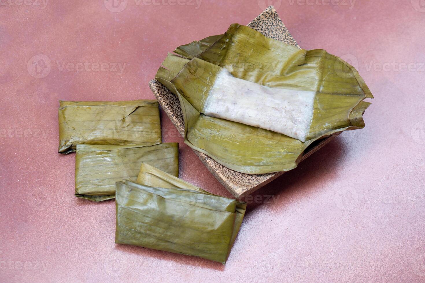 Steamed Banana Cake on a banana leaf. Placed on a plate with a coconut palm pattern. Wrapped banana cakes are lined up on the side. Placed on the red tile floor. photo