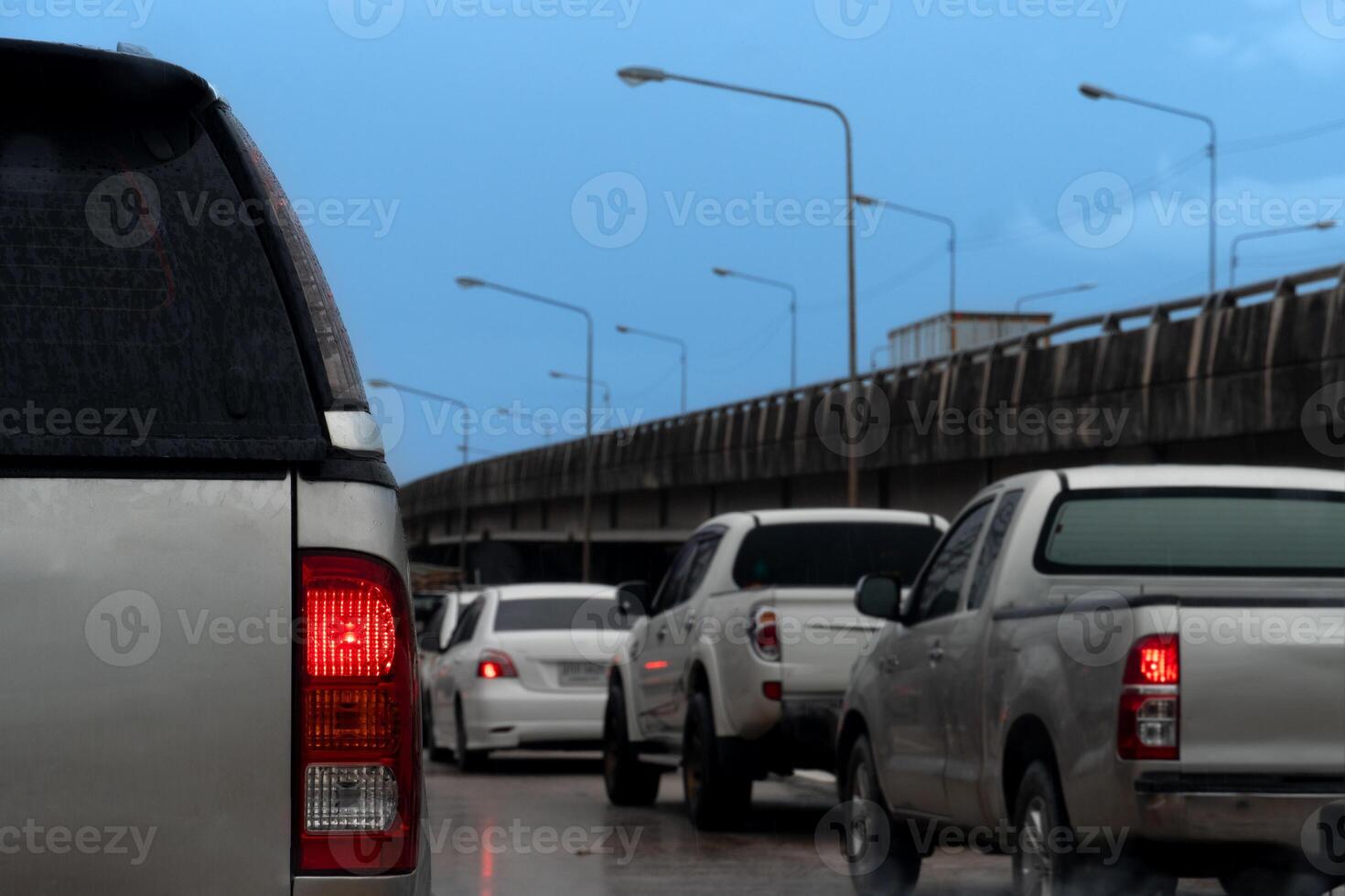 Rear side of dark car with on brake light. Parking on the road. Car is stained with rain stains. Cars are lined up on the road. And there is a concrete bridge on the side. with dark blue sky. photo