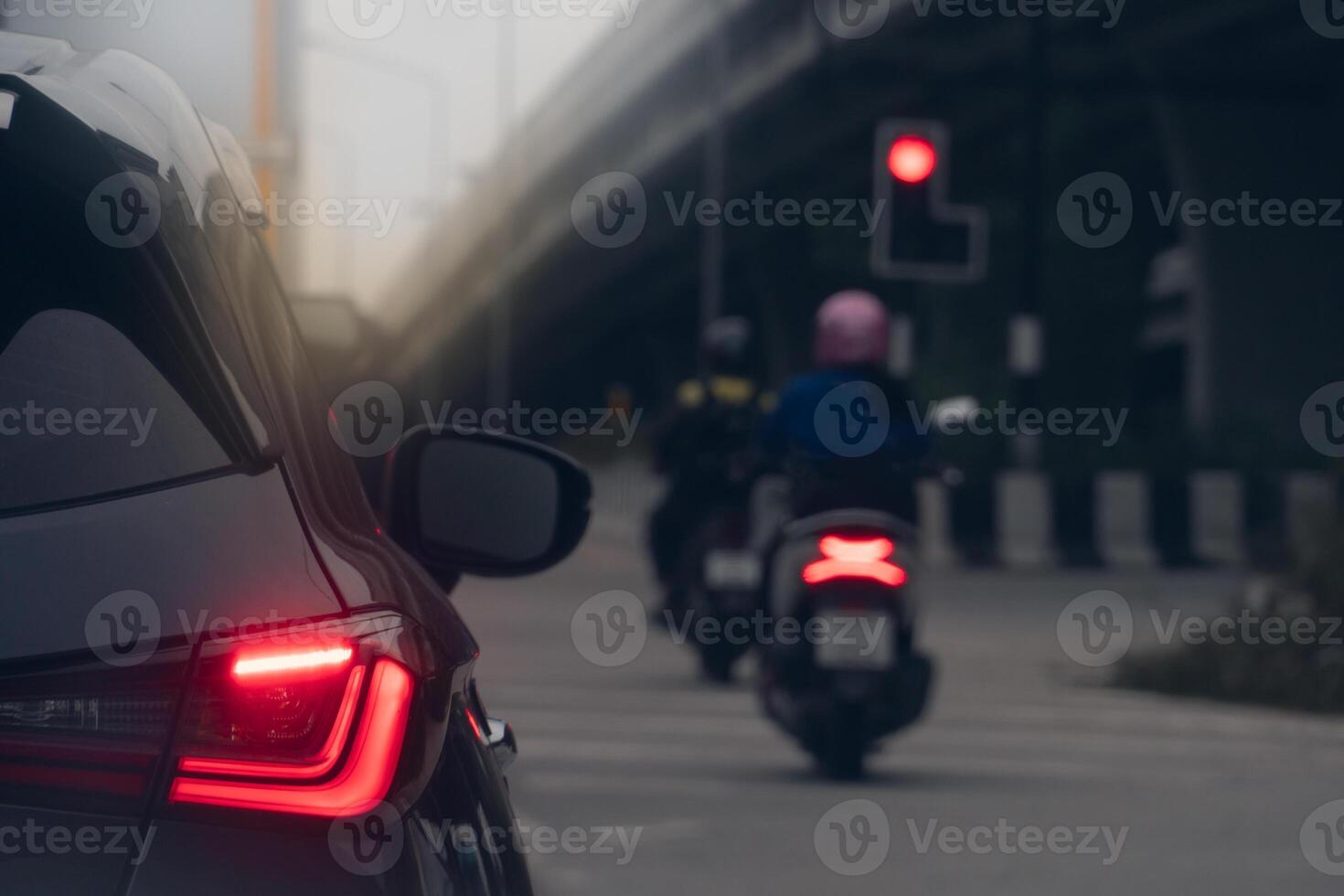 Rear side of dark car stop and turn on brake light. Motorcycle drives forward. Parallel concrete bridges are in front. Environment of traffic on the road at evening. photo
