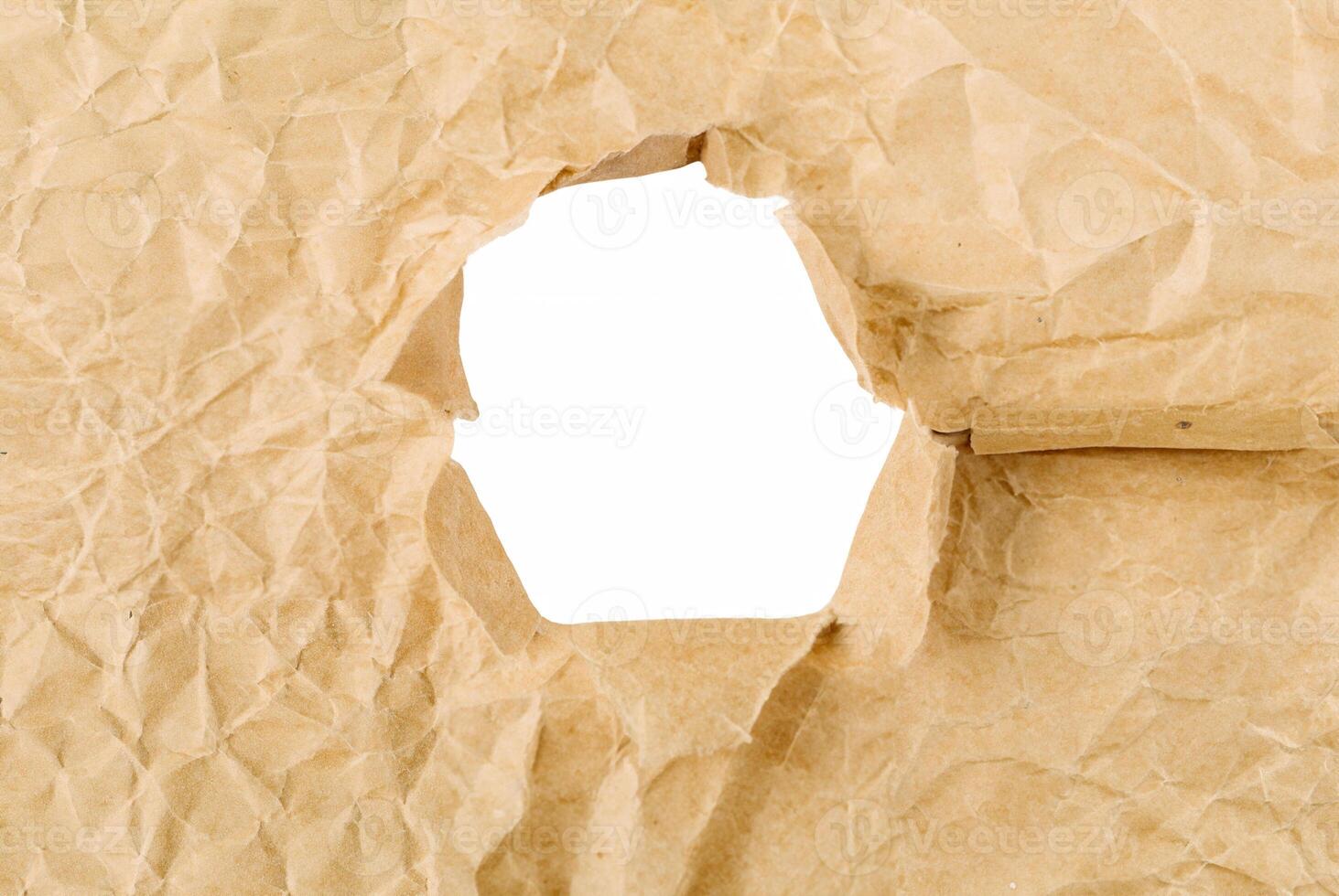 Close-up of crumpled brown paper with a torn hole, creating a frame effect on a white background, ideal for creative design use. photo