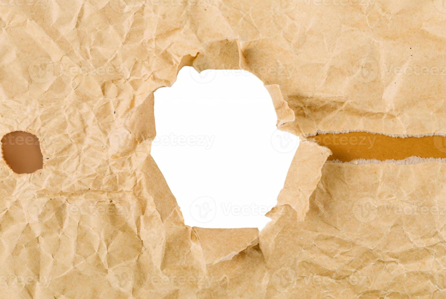 Close-up of crumpled brown paper with a torn hole, creating a frame effect on a white background, ideal for creative design use. photo