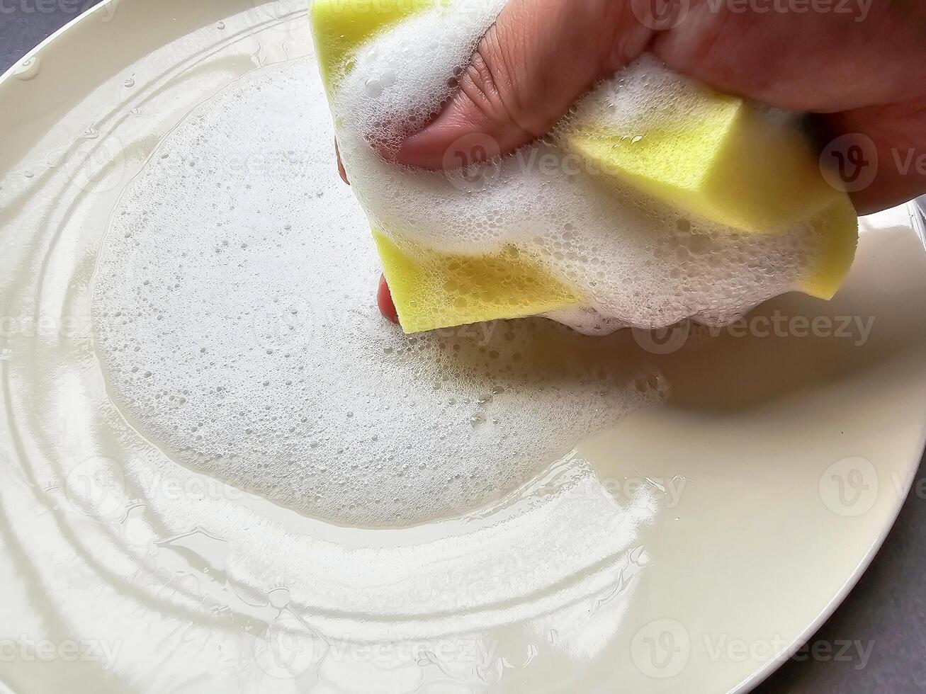hand gripping a sponge soaked in dishwashing liquid is commonly used for washing dishes. photo