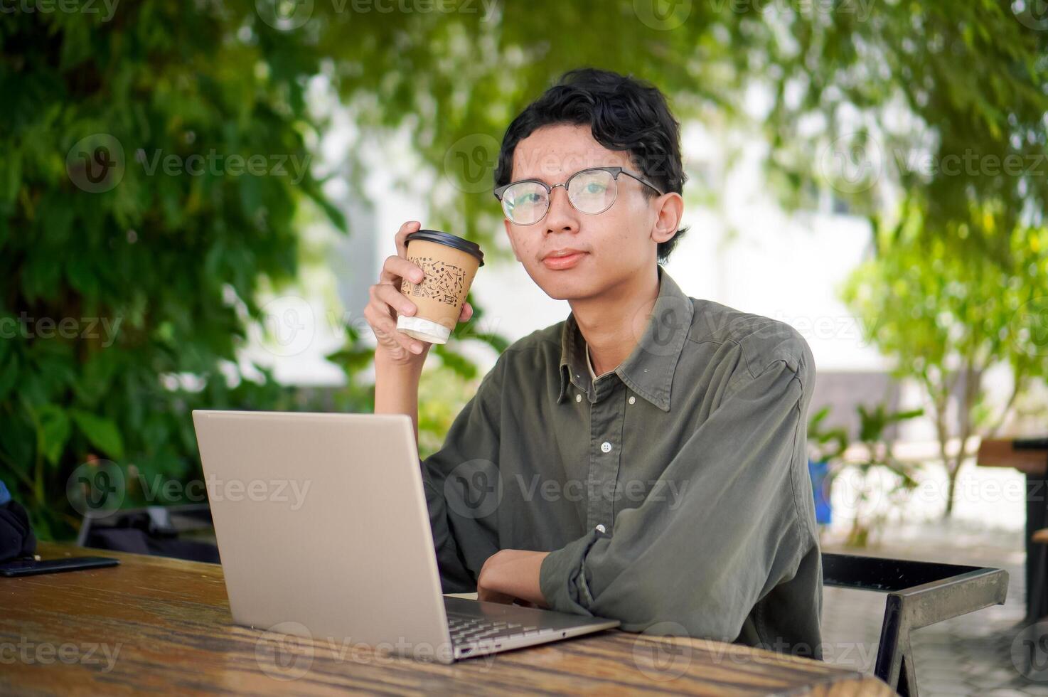 Asian man working on laptop at the outdoor cafe. A man working on laptop with a cup of coffee. photo