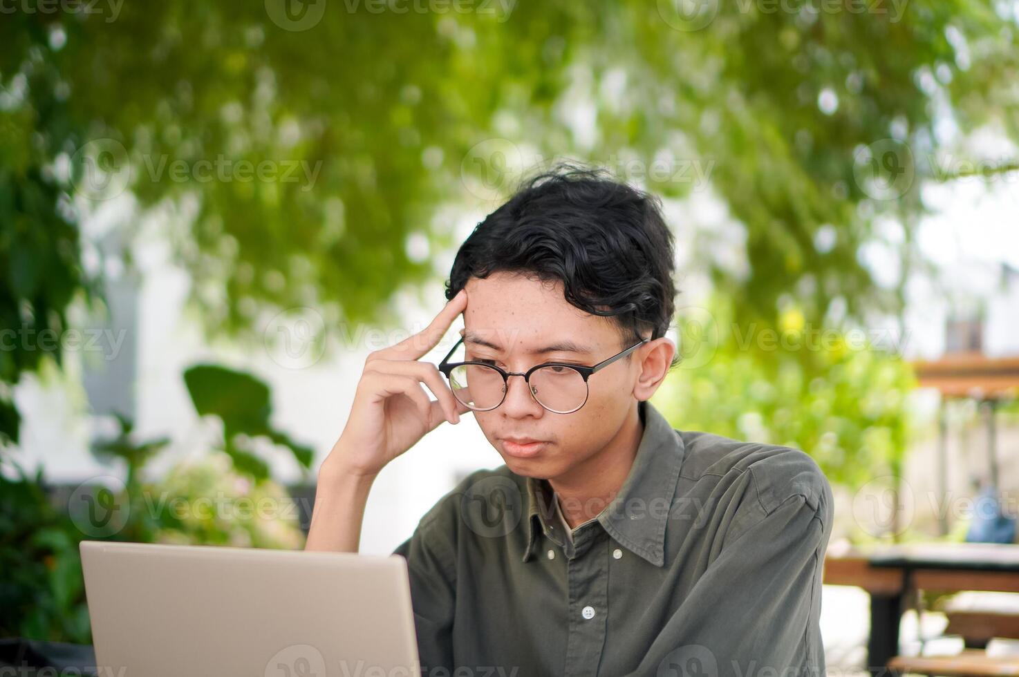 Young asian man thinking while looking to his laptop. Man working on his laptop at the outdoor cafe in the morning photo