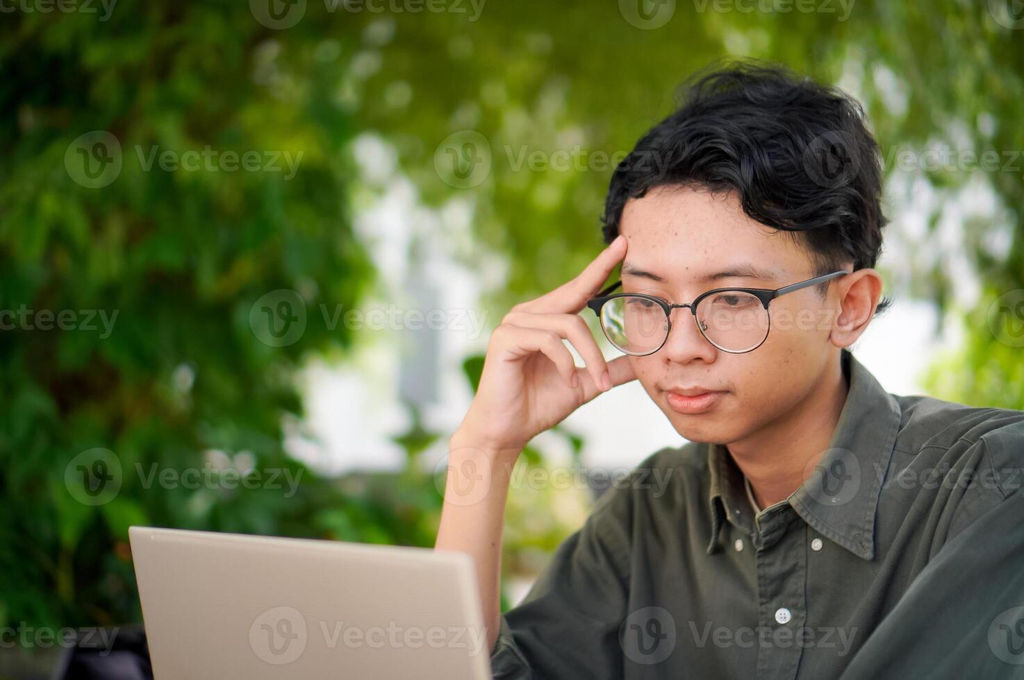 Young asian man thinking while looking to his laptop. Man working on his laptop at the outdoor cafe in the morning photo