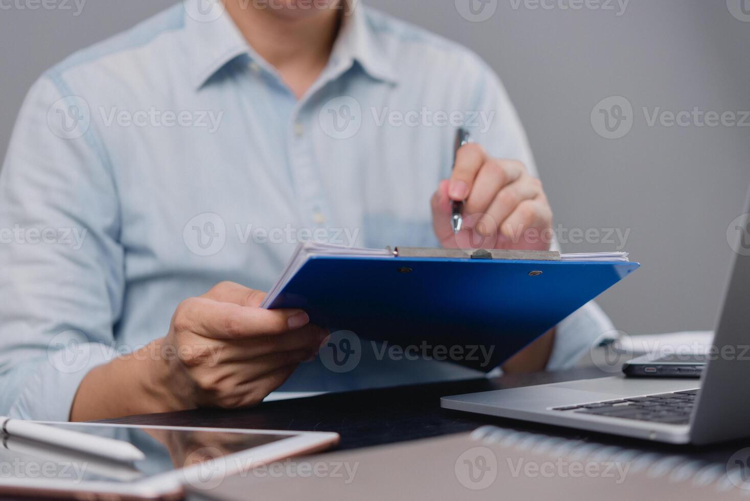 A man is writing on a clipboard while sitting at a desk photo