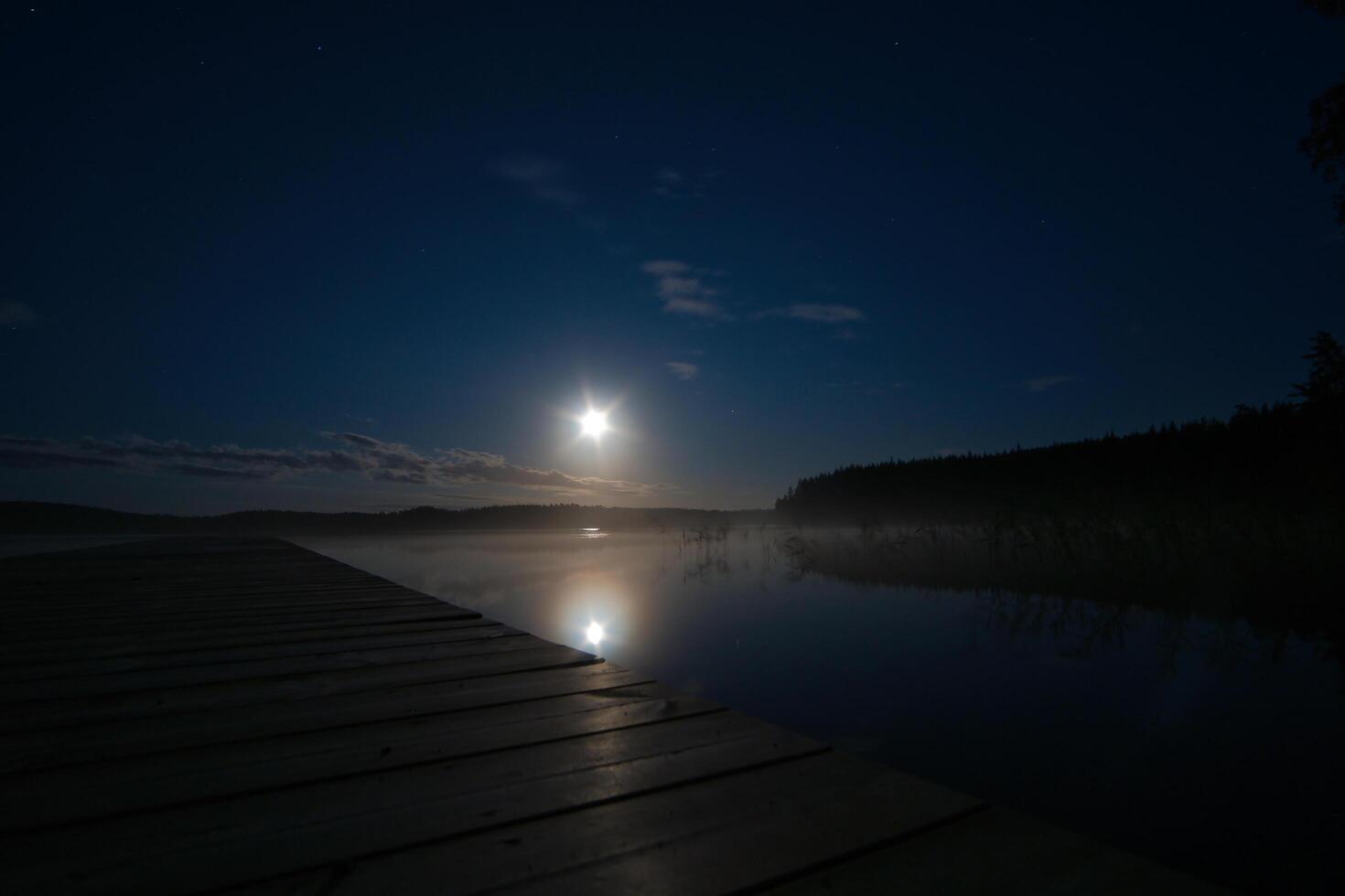 Moonlight over a lake in Sweden into which a wooden stay reaches. Scandinavian photo