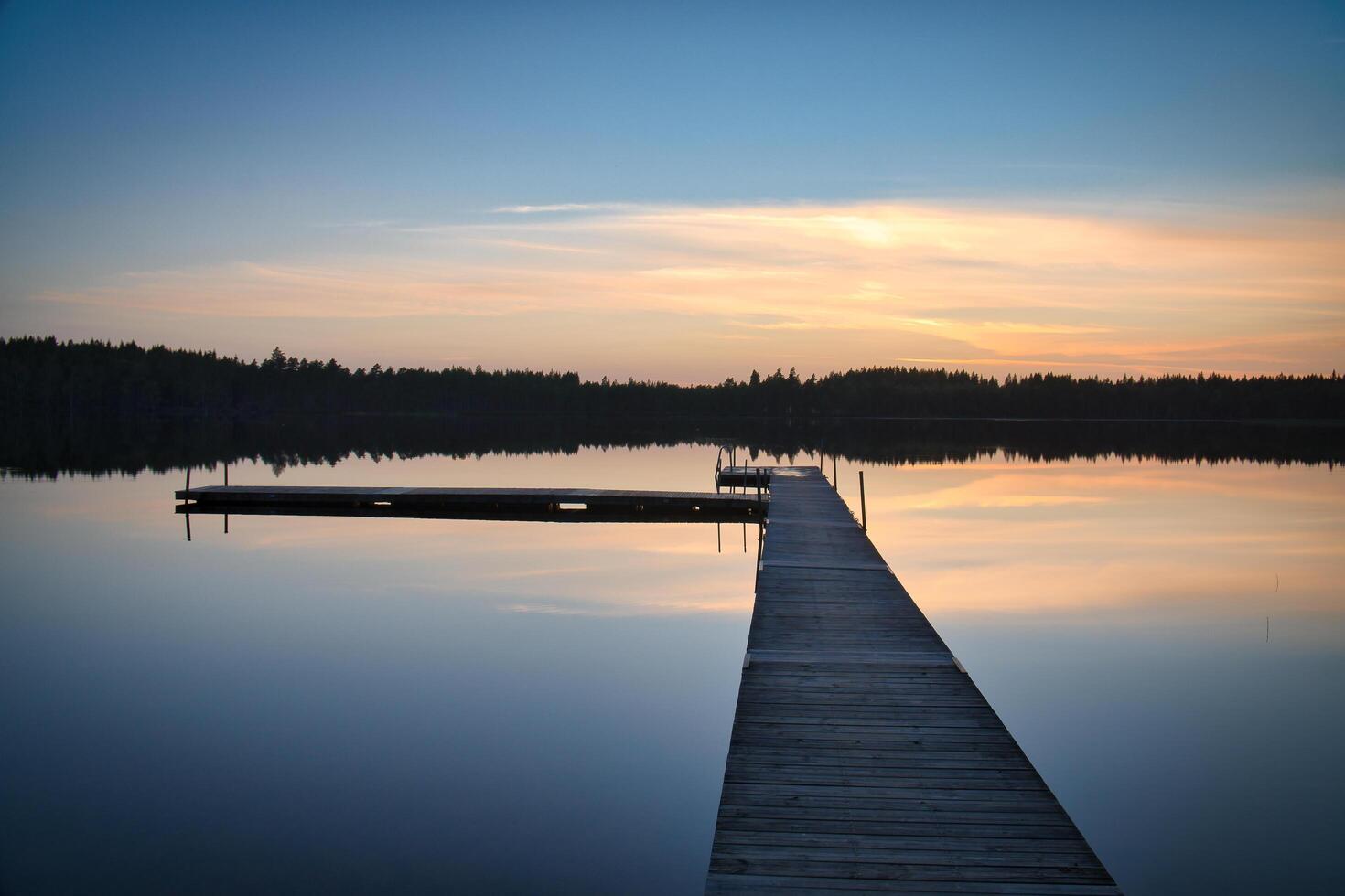 Wooden jetty at sunset on a Swedish lake. The colors are reflected in the water photo