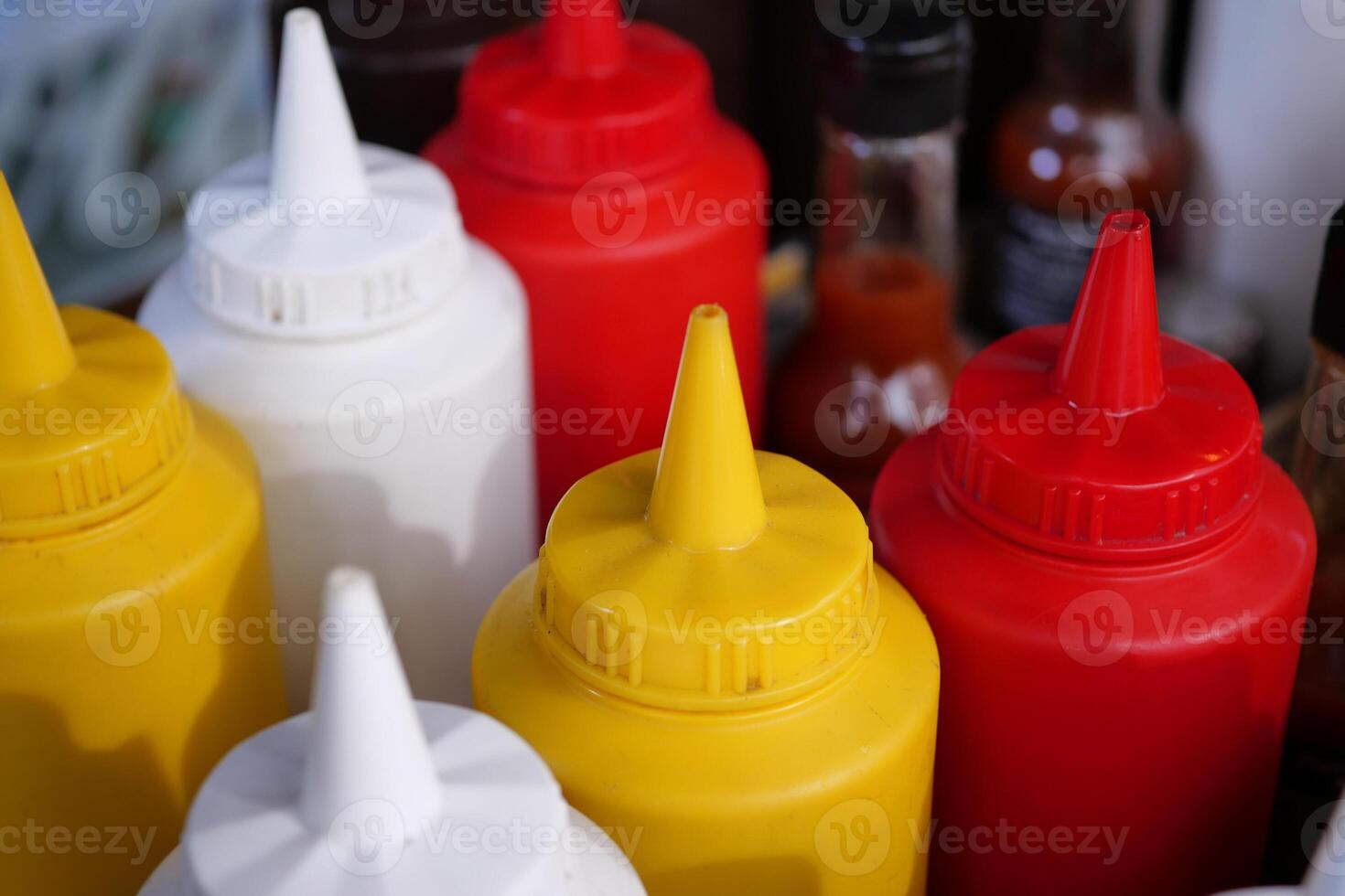 At a bustling food stand, a wide array of condiment bottles featuring vibrant colors can be found photo