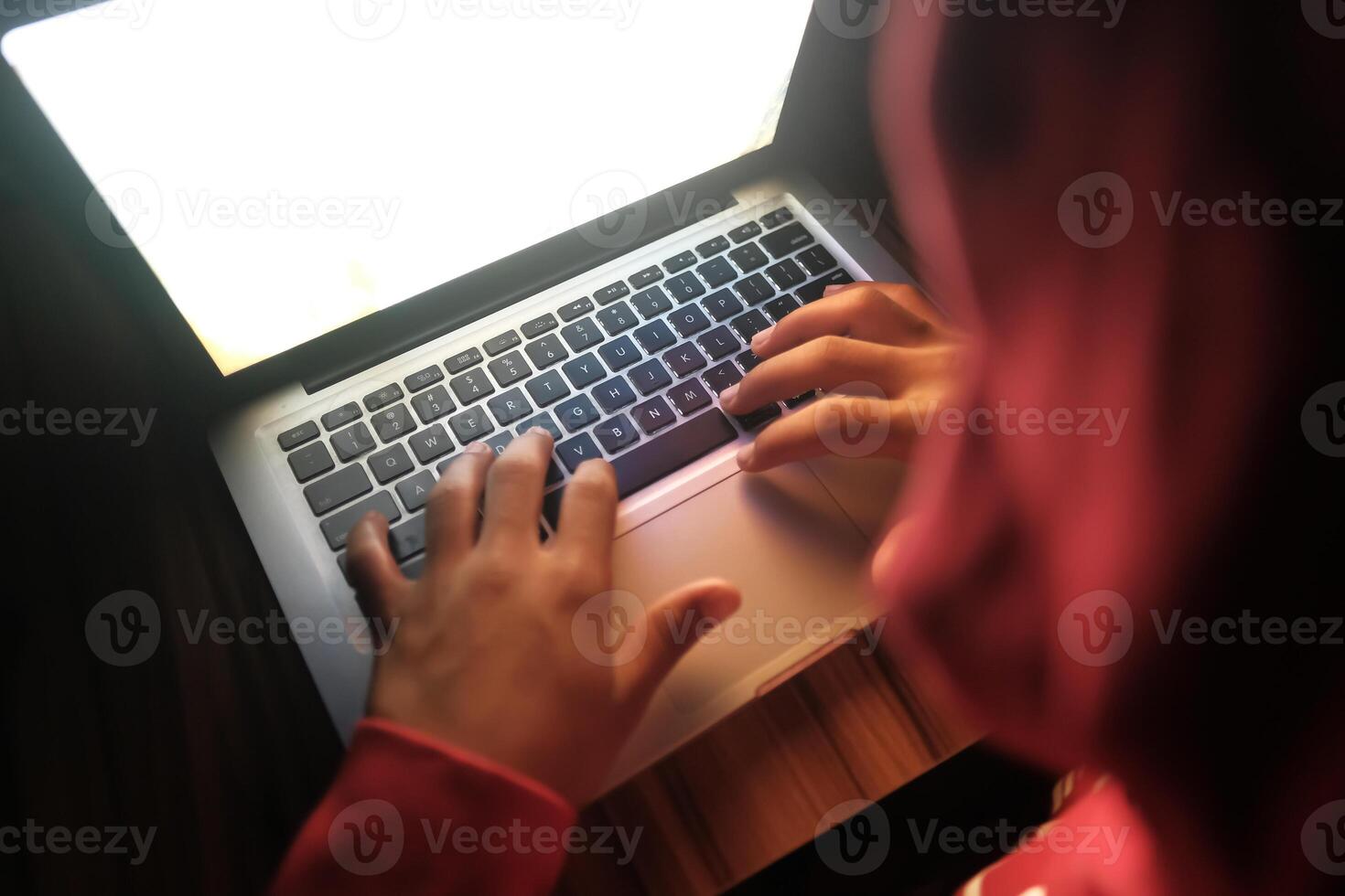 A person is intently focused on typing on a laptop while sitting in a dimly lit environment photo