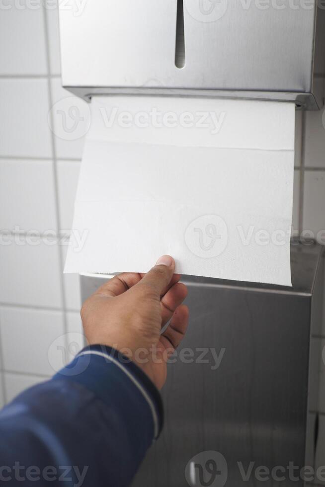 Hand Using Paper Towel Dispenser in a Hygienic Public Restroom with Clean White Tiles photo