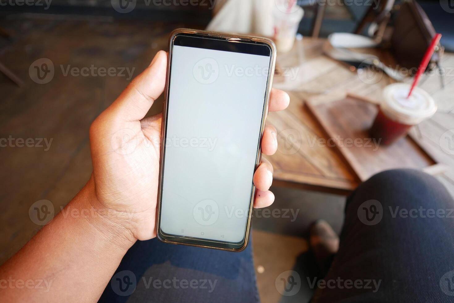 A person is holding a smartphone while sitting in a cozy coffee shop environment photo